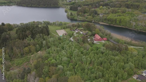  Aerial drone footage capturing the serene landscape of Stokka lake in Stavanger, Norway. The scene features a vast, calm body of water surrounded by lush greenery, captured at midday.