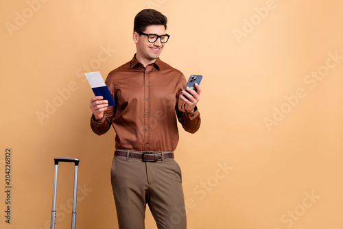 Fényképezés Young businessman checking smartphone with passport and boarding pass next to ca