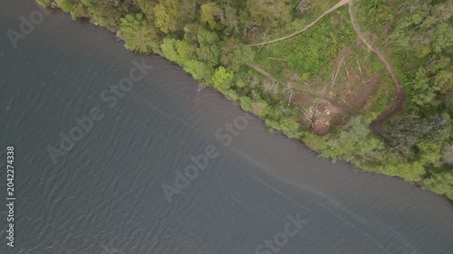  Aerial drone footage capturing the serene landscape of Stokka lake in Stavanger, Norway. The scene features a vast, calm body of water surrounded by lush greenery, captured at midday.