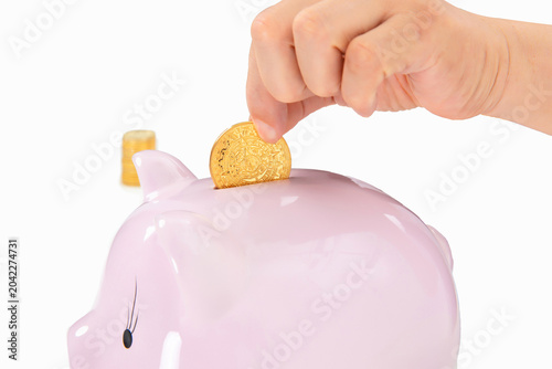 Tablou pe pânză Hand Putting Gold Coin into Pink Piggy Bank for Savings Concept