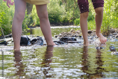 Children standing barefoot in shallow stream on summer day. Depersonalized photo