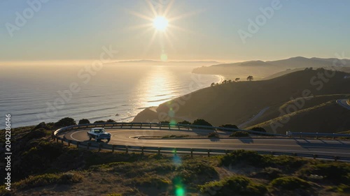 Aerial View of Classic Car Driving Winding Coastal Highway Illustrating Freedom and Scenic Road Trip at Golden Hour