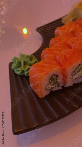 A female hand slowly rotates a black serving plate with Philadelphia sushi, ginger and wasabi. Red ambient lighting creates a stylish and cozy restaurant mood