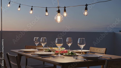 Festive dining table set with string lights illustrating an intimate evening gathering on a rooftop at dusk.