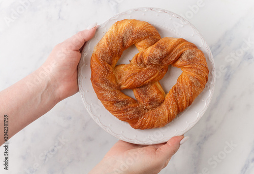 Homemade puff pastry pretzel with sugar and cinnamon on a white plate on a marble table. Selective focus, top view
