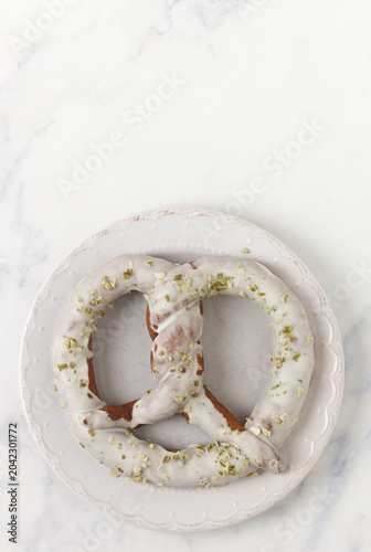 Homemade chocolate pretzel with white chocolate and pistachios on a white plate on a marble table. Selective focus, copy space, top view