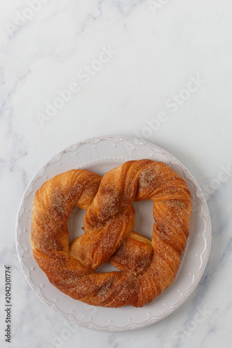 Homemade puff pastry pretzel with sugar and cinnamon on a white plate on a marble table. Selective focus, top view, copy space,