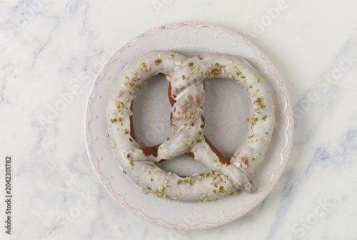 Homemade chocolate pretzel with white chocolate and pistachios on a white plate on a marble table. Selective focus, copy space, top view