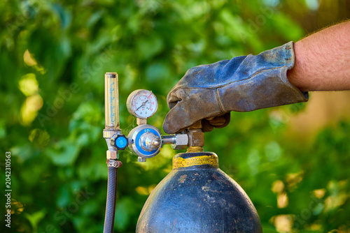 Fotografie Close-up of protective gloved hand adjusting oxygen gas cylinder regulator outdo
