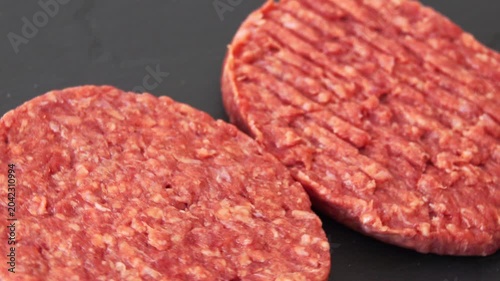 Two raw beef patties on black surface