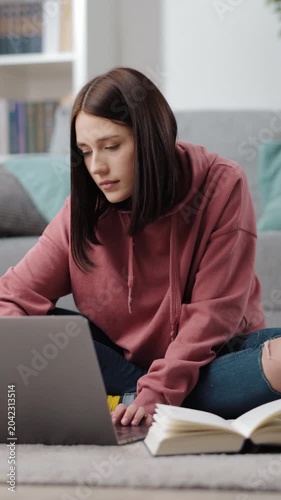 Woman studies on laptop at home in a cozy setting with books around her.