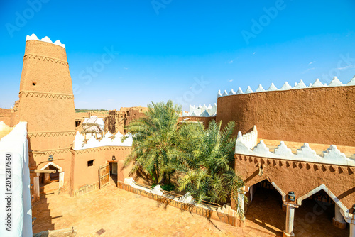 Ushaiqer Heritage Village entrance with a weathered wooden door and traditional lock opening to a courtyard of mud-brick walls, and a distinctive support pillar in Najdi style of Saudi Arabia