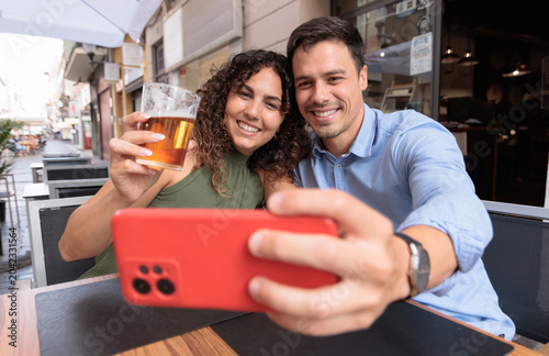 Billede på lærred A man and a woman taking a selfie while having a beer at a restaurant