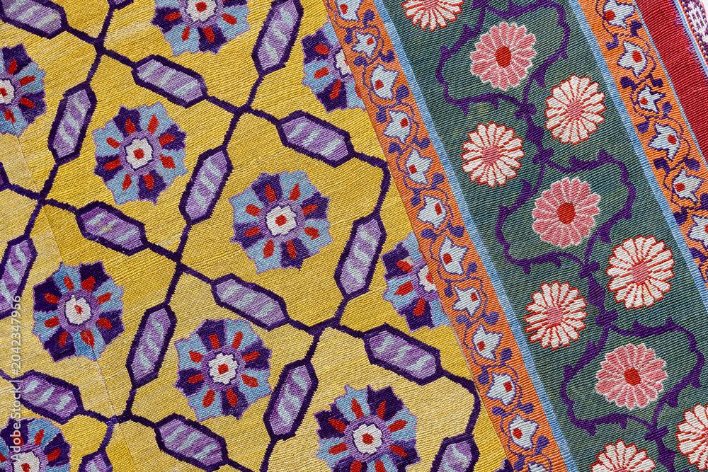 Fototapeta premium Vibrant woven rug featuring intricate floral motifs and geometric lattice on bold yellow and green bands. Ornate decorative textile evokes traditional craftsmanship