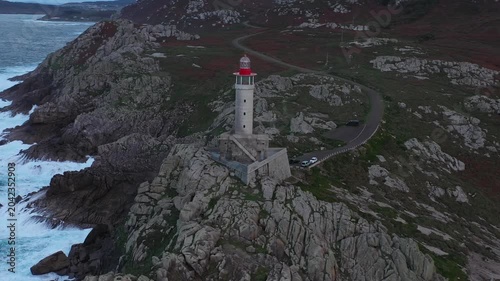 Aerial view of Faro de Punta Nariga lighthouse standing on rugged rocky cliffs along the Atlantic coast in Malpica, A Coruna, Spain.