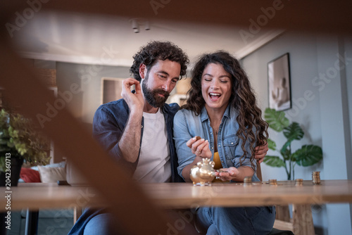 Fotografie Happy couple saving money in a piggy bank at home