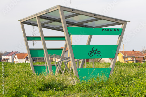 Modern Green Covered Bike Parking Shelter With Bicycle Rack In Suburban Field Near Houses