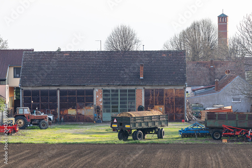 Obraz na płótnie Rural Farmyard With Old Barn, Tractors and Trailers Near Plowed Field in Country