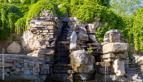 Photography Rustic rock waterfall with cascading water and lush ivy in a landscaped garden