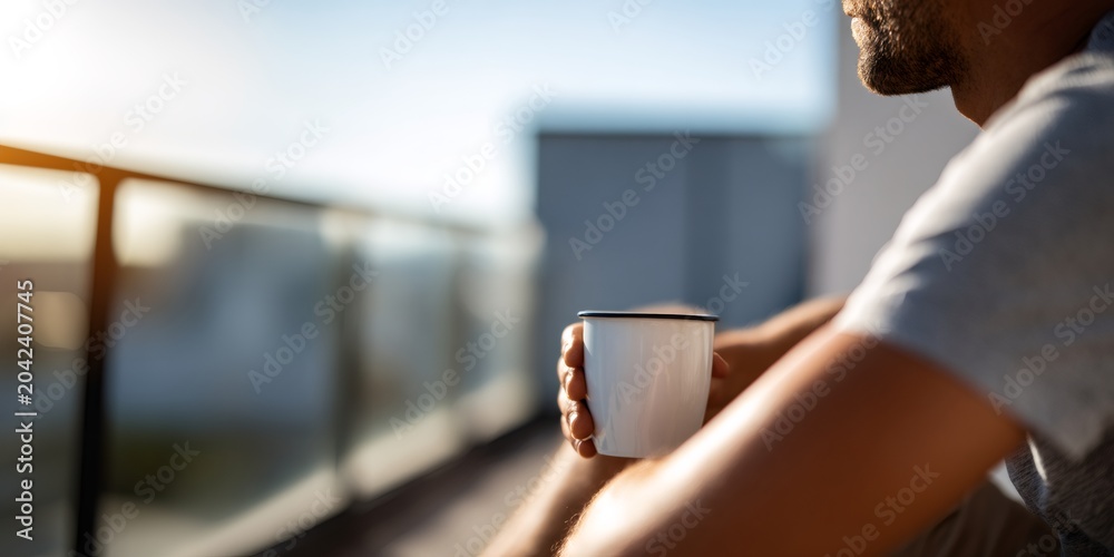 Obraz premium Close-up of a man holding a coffee cup on a sunny balcony. Relaxing morning break in the city