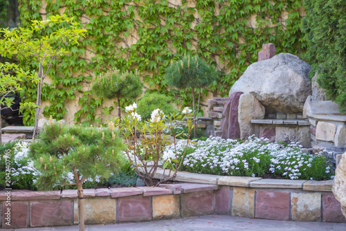 Foto Tranquil backyard garden with rock bench, white flower bed and ivy-covered wall