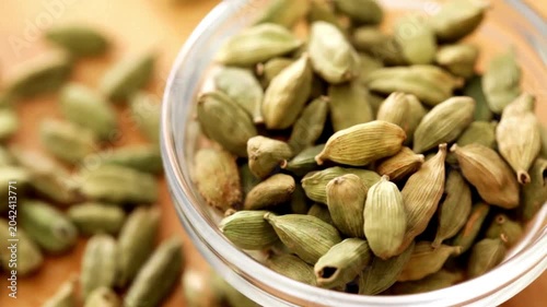 Macro close-up of green cardamom pods in a small glass bowl on a wooden surface