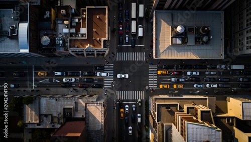 Obraz na płótnie Directly overhead aerial view of a busy urban intersection at warm sunset showing yellow taxis, trucks, pedestrians on crosswalks, long shadows, and building rooftop details