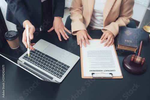Schilderij op canvas Legal Consultation: Two individuals are reviewing a contract at a desk, with a laptop, gavel, and law book in view, signifying a legal discussion and contract agreement