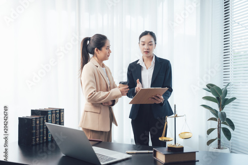 Legal Consultation: Two professional women, likely lawyers or paralegals, are engaged in a serious discussion in an office setting.