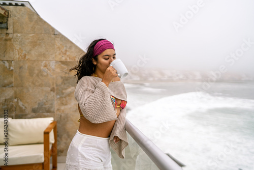 Tableau sur toile Young woman enjoying morning beverage on oceanfront balcony