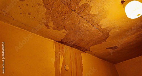 Fotografie Water damage and stains on a textured ceiling and wall with a light fixture