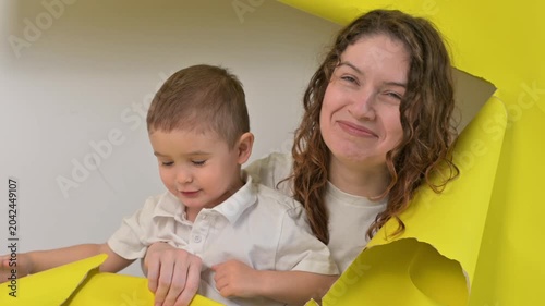 Caucasian little boy and his mother tearing yellow paper background. 