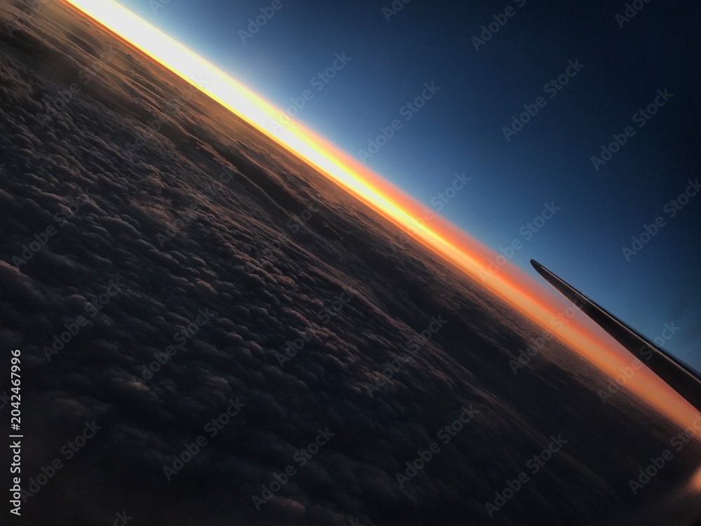 Fototapeta premium Sunset above the clouds view from airplane window A breathtaking view of a vibrant golden sunset above a thick layer of clouds, taken from a commercial airplane window with a wing
