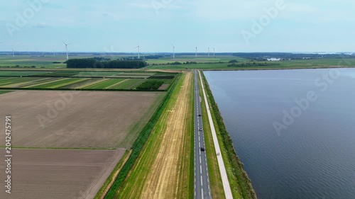 Road with cars driving next to water in agriculture landscape.