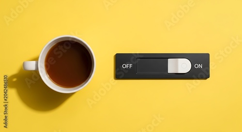 A white cup of black coffee next to a black electronic switch set to the off position on a vibrant yellow background, for morning motivation