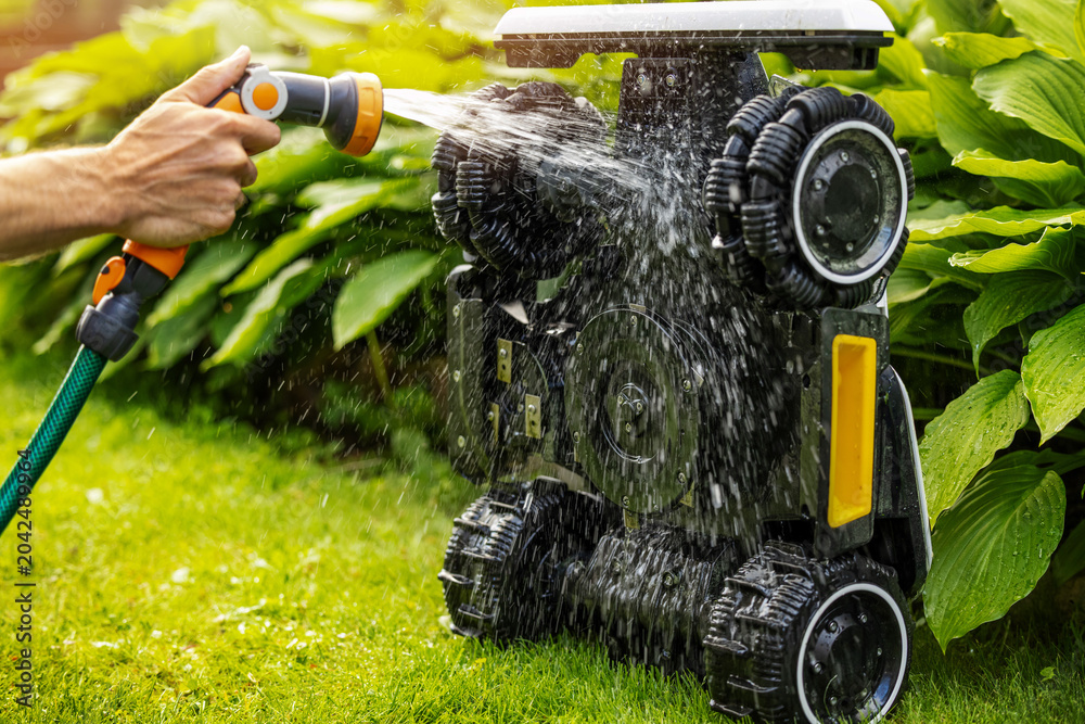 Fototapeta premium Cleaning robotic lawn mower. Washing with water from garden hose