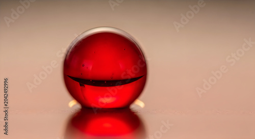 Red glass marble ball with a reflection on a smooth glossy surface, close-up macro shot.