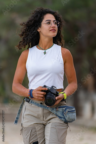 Young female photographer walking with camera in ancient ruins or nature park.