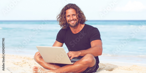 Smiling man using laptop on sandy beach
