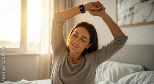 Woman stretching in bed wearing a smartwatch to track sleep quality. Concept of morning wellness, healthy lifestyle and digital health technology monitoring in the bedroom at sunrise.