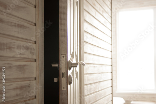 A slightly open interior door with a doorknob and light from a window illuminates the room for the themes of entry, exit, door opening, room access
