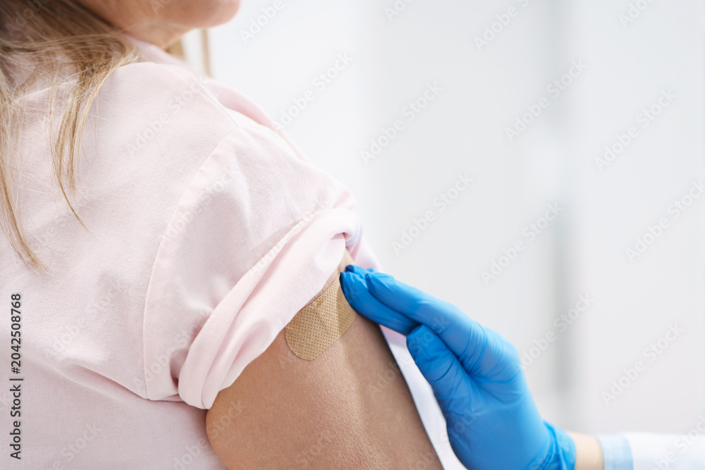 Fototapeta premium Doctor in medical gloves applying adhesive bandage onto patient's arm after vaccination in hospital, closeup