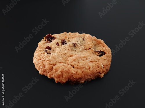 Close-up of a round oatmeal and raisin cookie with a rustic, golden texture. Cookie isolated on a black background. Homemade desserts and pastries. Healthy eating.