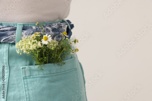 Woman with flowers in her pocket on light grey background, closeup. Space for...