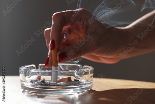 Fotografía Woman putting out cigarette in ashtray at wooden table, closeup