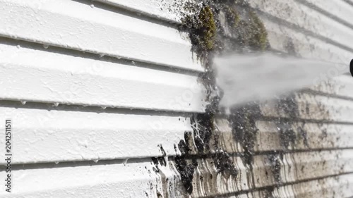 Pressure washing dirty white vinyl siding of a house