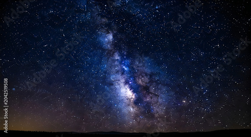 Bright milky way galaxy shining with countless shimmering stars in the deep dark blue night sky above the quiet horizon