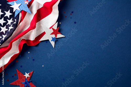 American flag draped on the left and patriotic red, white, and blue glitter stars. Navy blue textured background with copy space for 4th of July or Memorial Day.