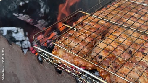 Tender meat ribs cooking on metal grill over glowing coals with smoke and flames during relaxing outdoor barbecue gathering in nature.