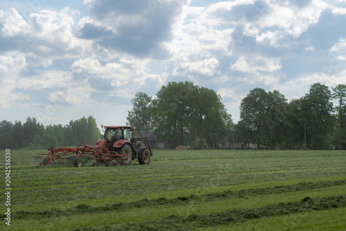Photos Tractor raking hay in green rural farm field under dramatic cloudy summer sky